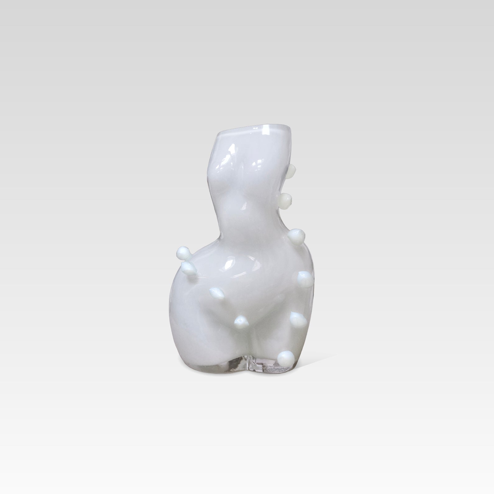 White glass sculpture of a womans figure, with bubble-like spots around it, on a light gray background
