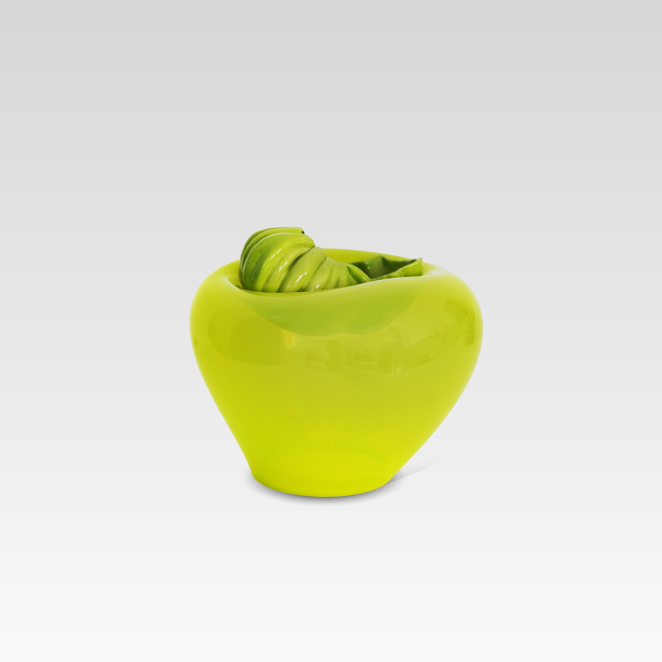 A bright lime green glass vessel or bowl shaped like a stylized apple, featuring a textured green detail resting on top, set against a light gray gradient background