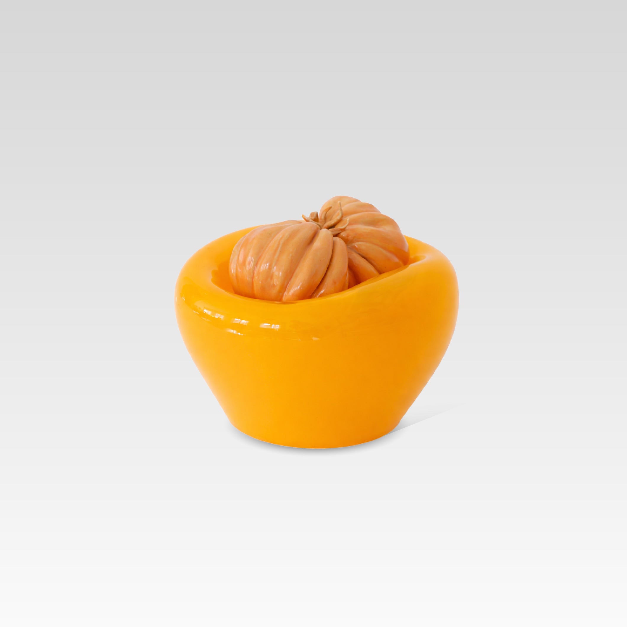 An orange-colored glass vessel or bowl with a sculpted ceramic orange tomato detail on top, set against a clean light gray gradient background