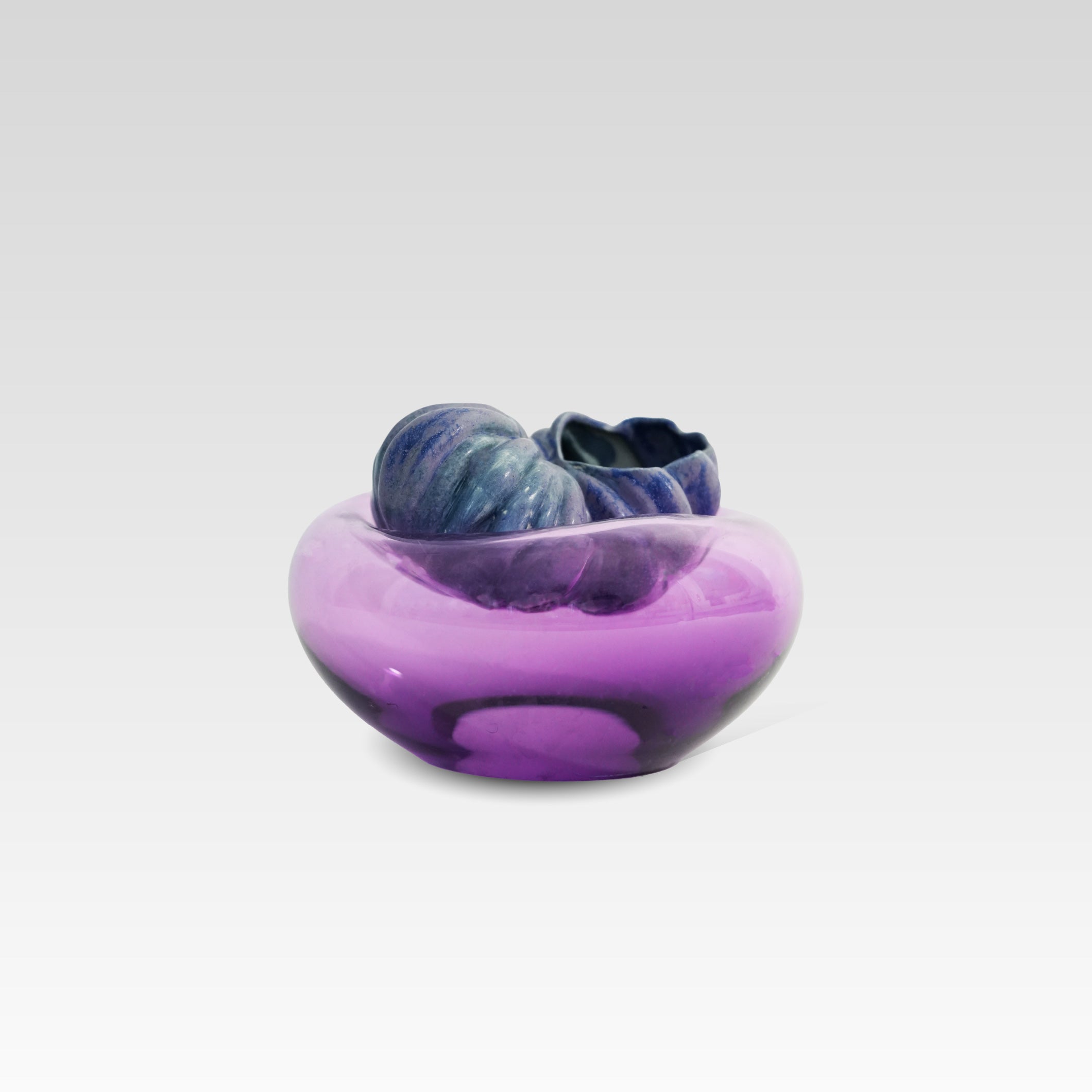 A sculptural glass vessel or bowl with a dark blue spiral shell-like, hollow, tomato form resting on the top