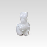 White glass sculpture of a womans figure, with bubble-like spots around it, on a light gray background