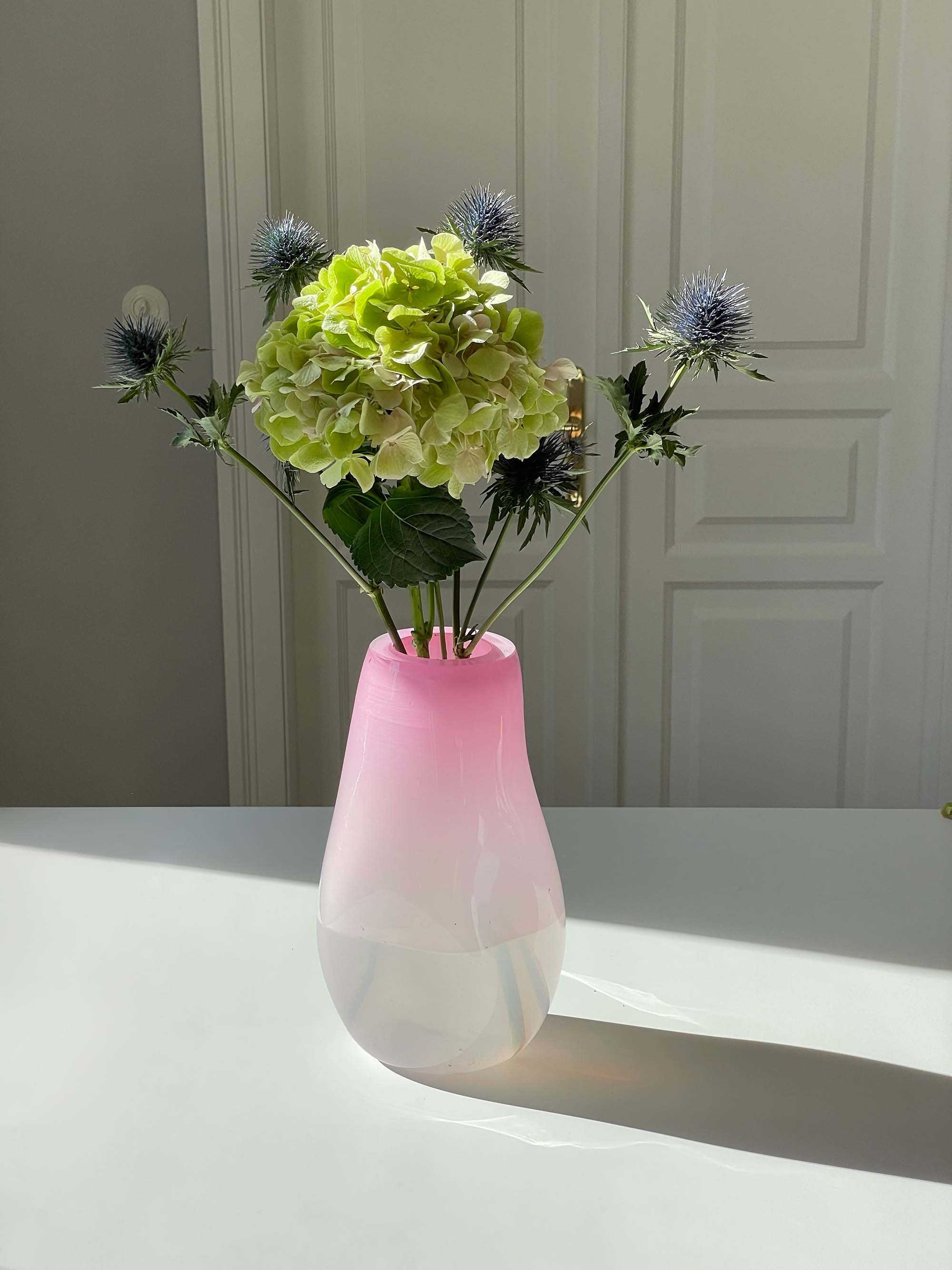 Pink and white vase with flowers on a table against a neutral wall