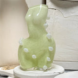 Futura cloud limoncello coloured womans figure, glass vase, with white blob dots on a white surface in a workshop context.