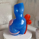 Blue and red sculpture on a white pedestal against a textured wall.
