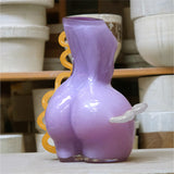 Purple futura waves glass vase on a clean surface with ceramic pots in the background.