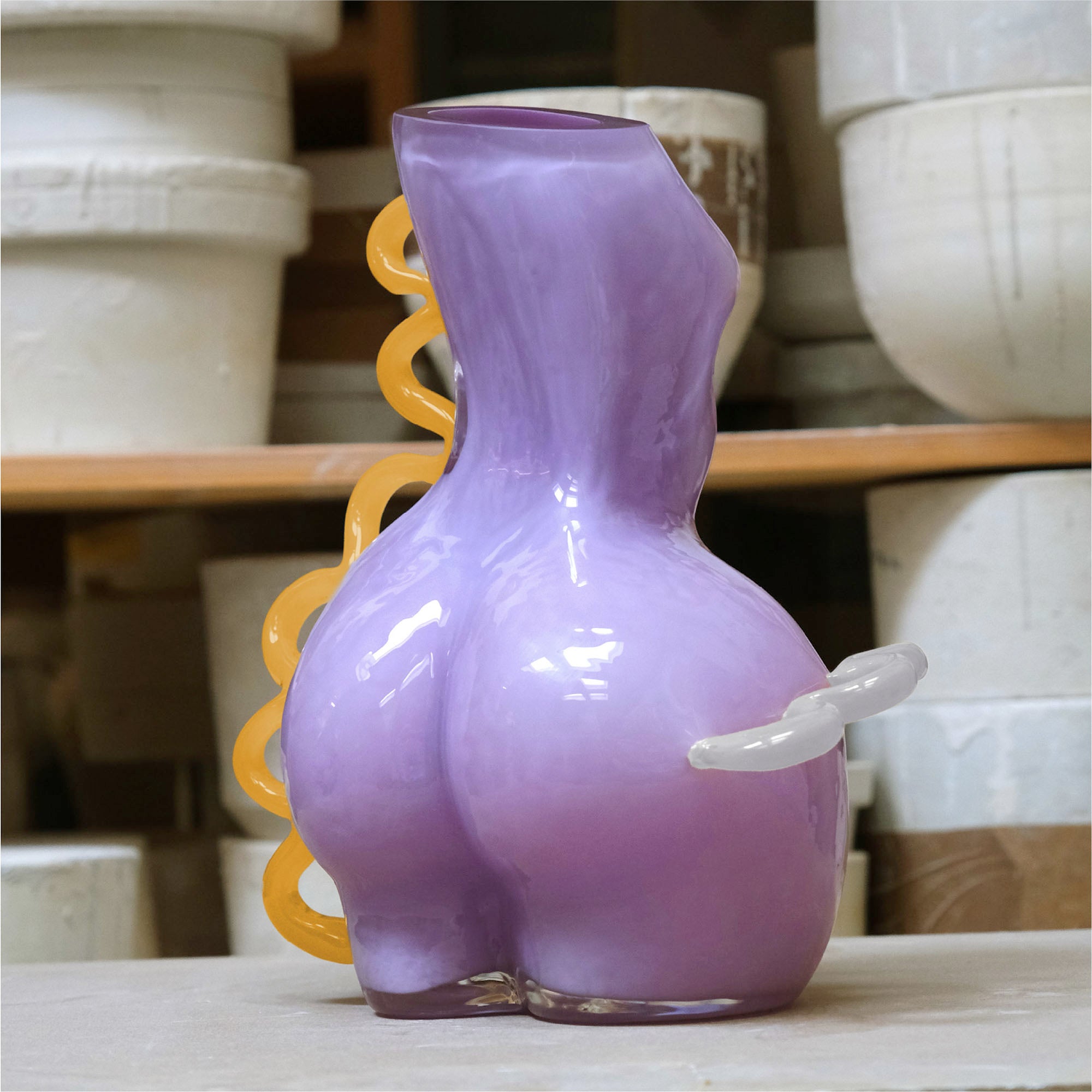 Purple futura waves glass vase on a clean surface with ceramic pots in the background.