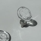Clear glass cabinet knob on a gray background, light shining through it.