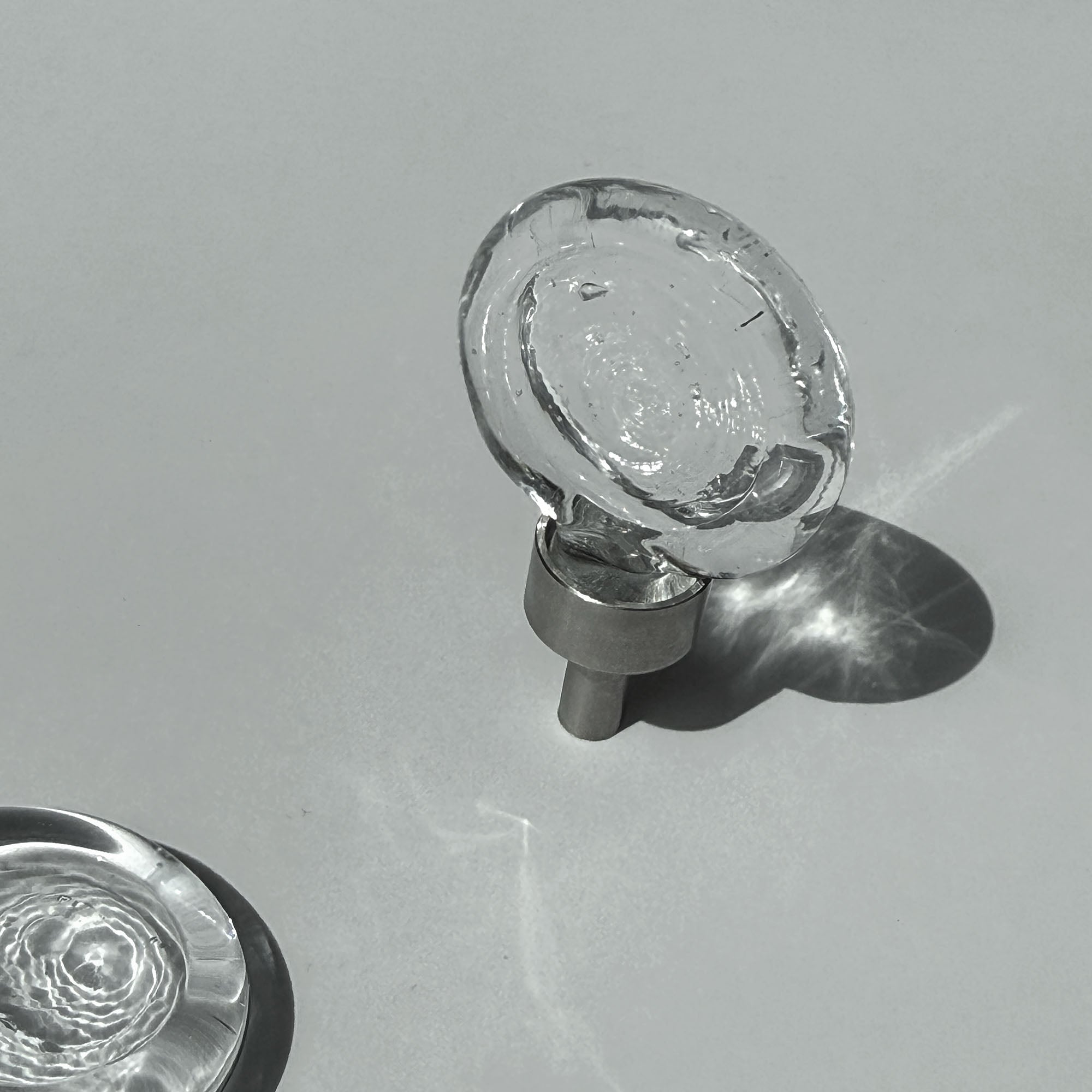 Clear glass cabinet knob on a gray background, light shining through it.