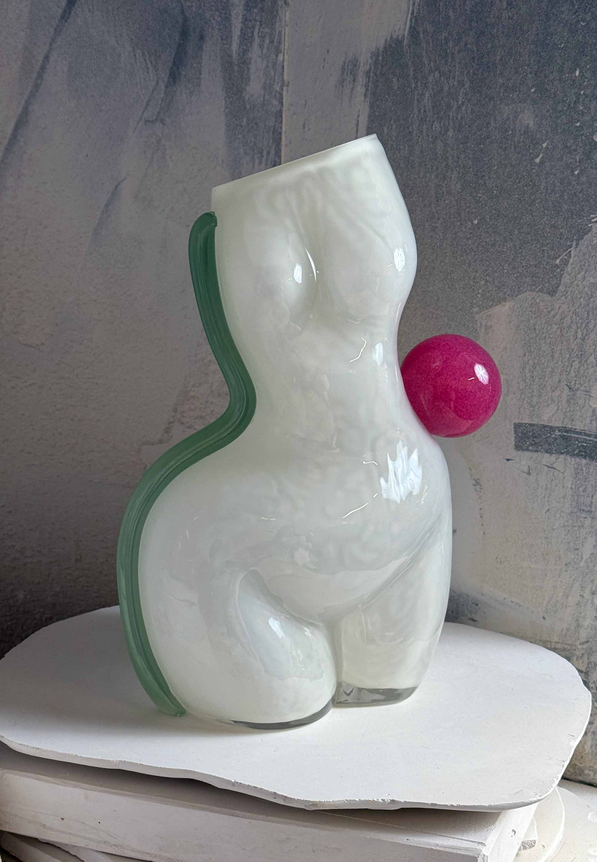 Glass sculpture of a nude figure with a pink object on a gray surface