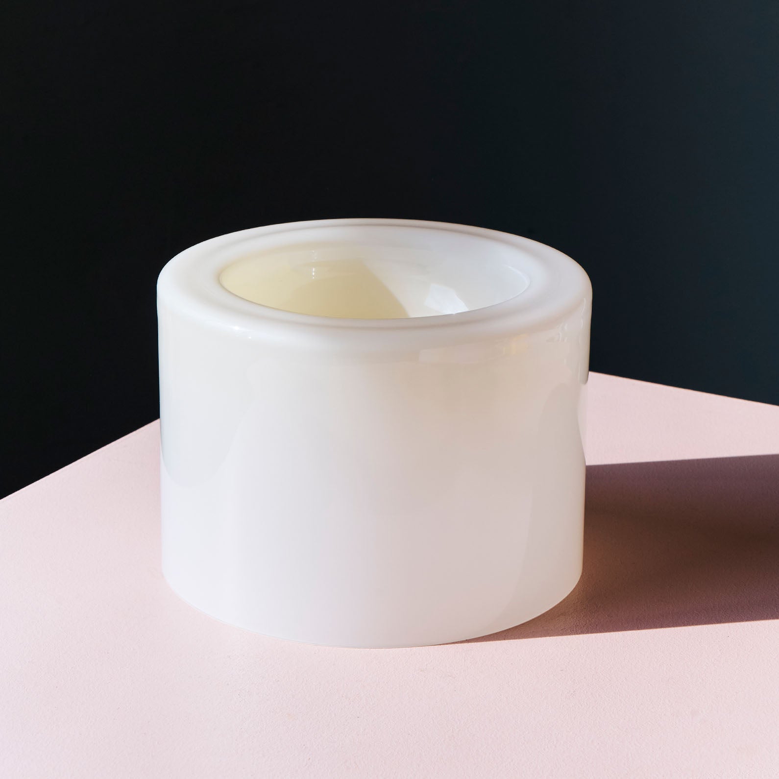 A high vanilla bowl placed at the corner of a soft pink table against a dark wall in the background.