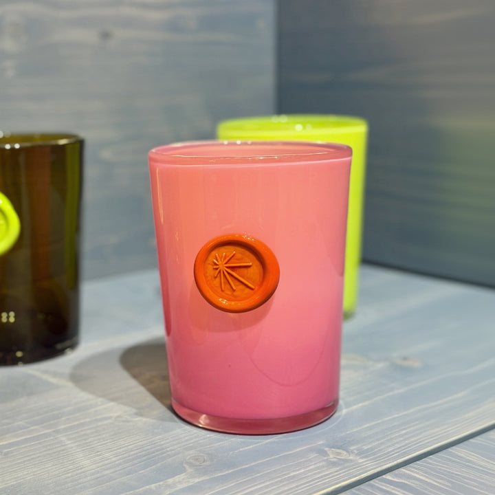 Set of colorful glass vases with a pink one featured in the middle with an orange circular imprint, placed on a wooden surface.
