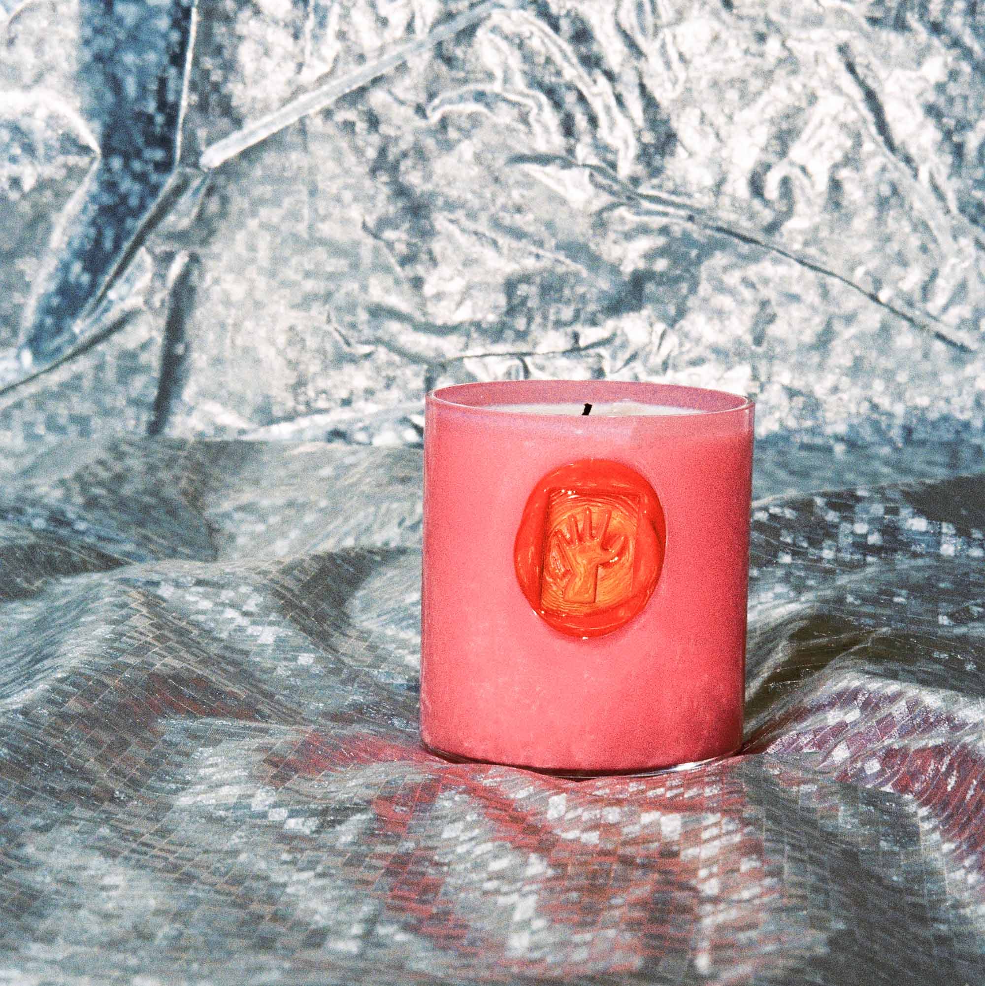 Pink candle with a decorative orange-red seal on a textured surface