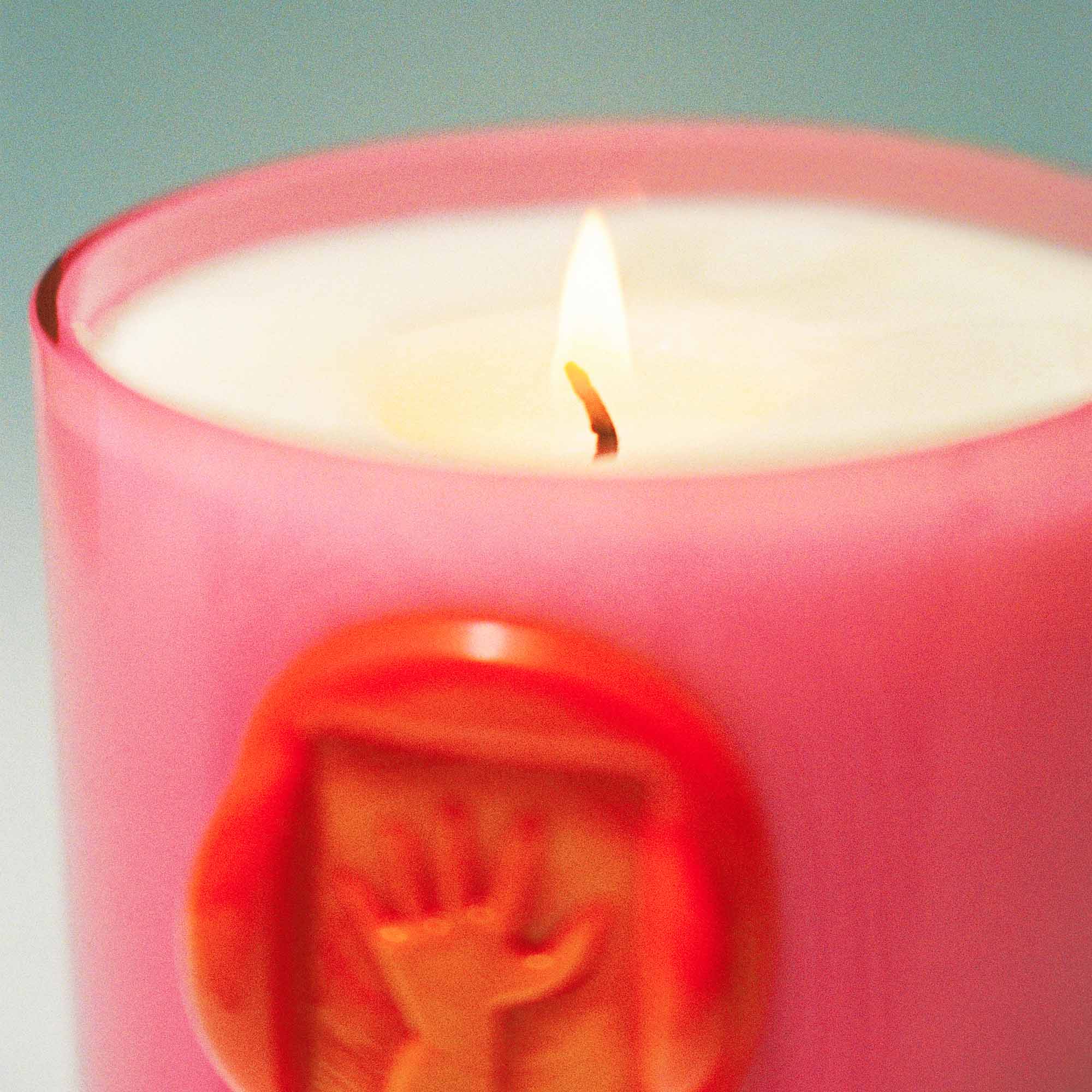 Pink candle that is lit, with a hand seal design on a gray background