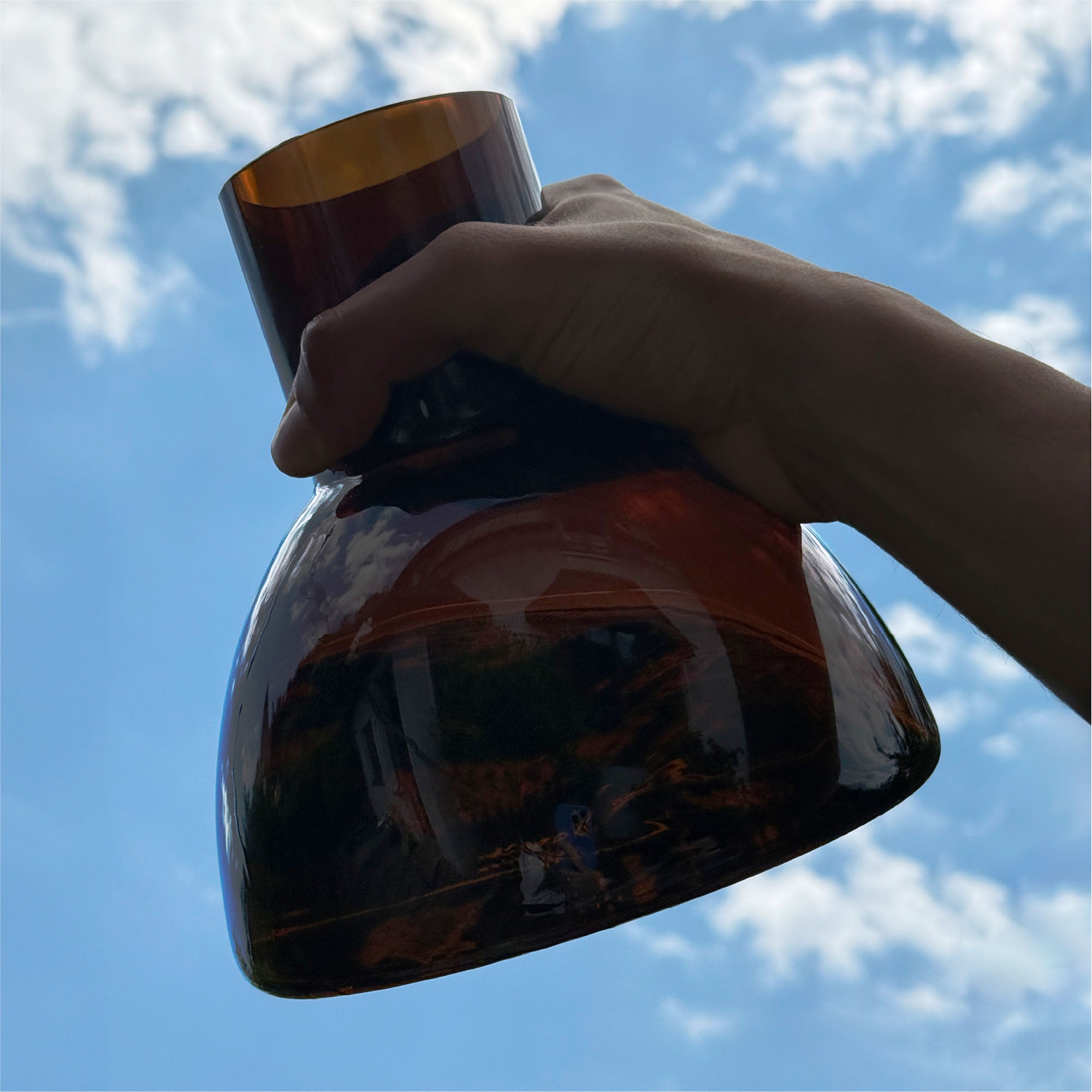 A hand is holding the neck of the plash carafe and the background view is of the blue sky.