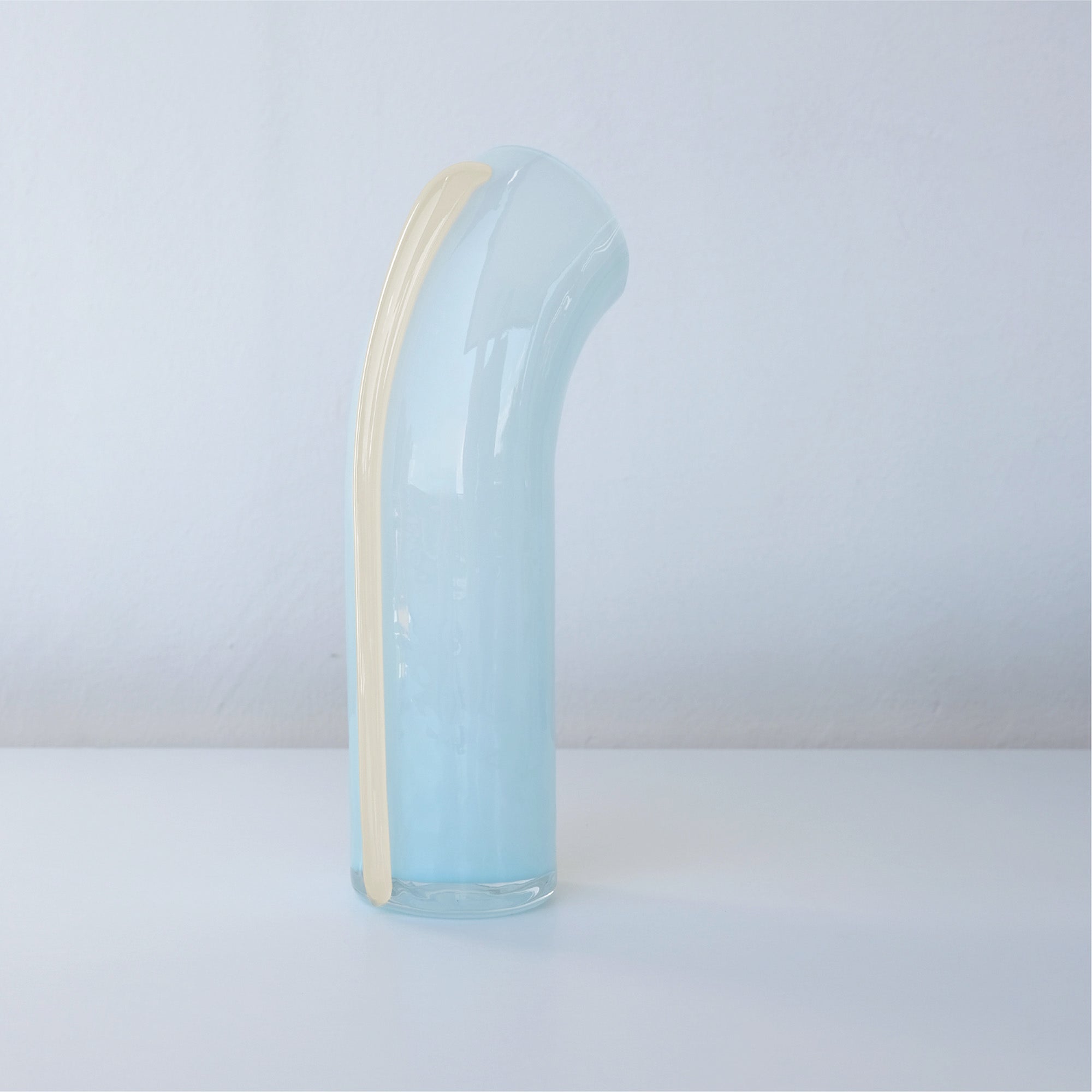 Soft blue nessie with a vanilla stripe on the back, curved object, on a light gray background, facing away from the camera to see the back view of Nessie.