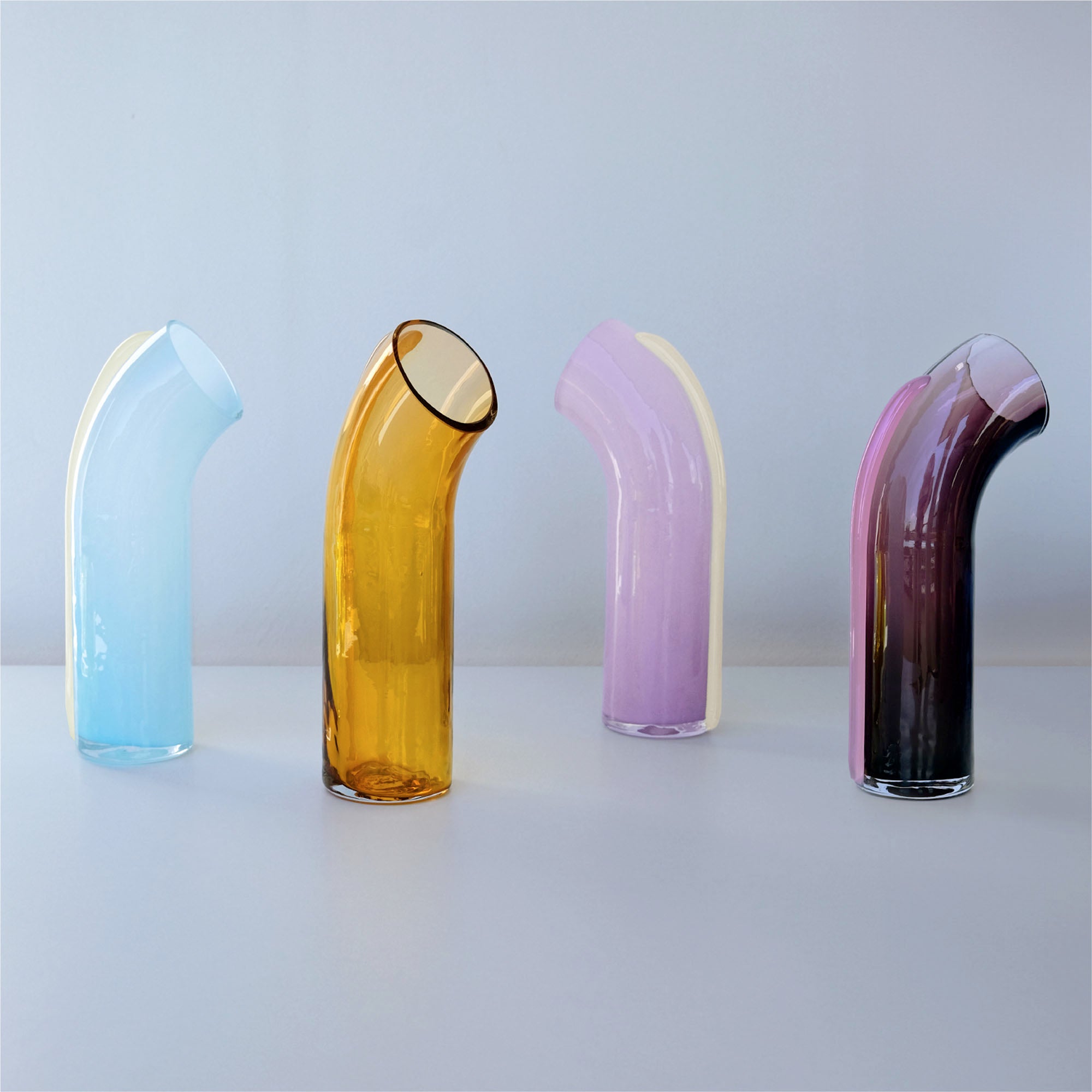 Four colorful glass Nessie vases on a white surface with a light blue background.