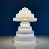 Pulsar table lamp with wavy form, positioned on a soft reflective surface with a dark blue background.