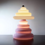 Pulsar lamp transitioning from a soft pink on the bottom to a vanilla on the top. In a moody setting on a dark surface with grey background.