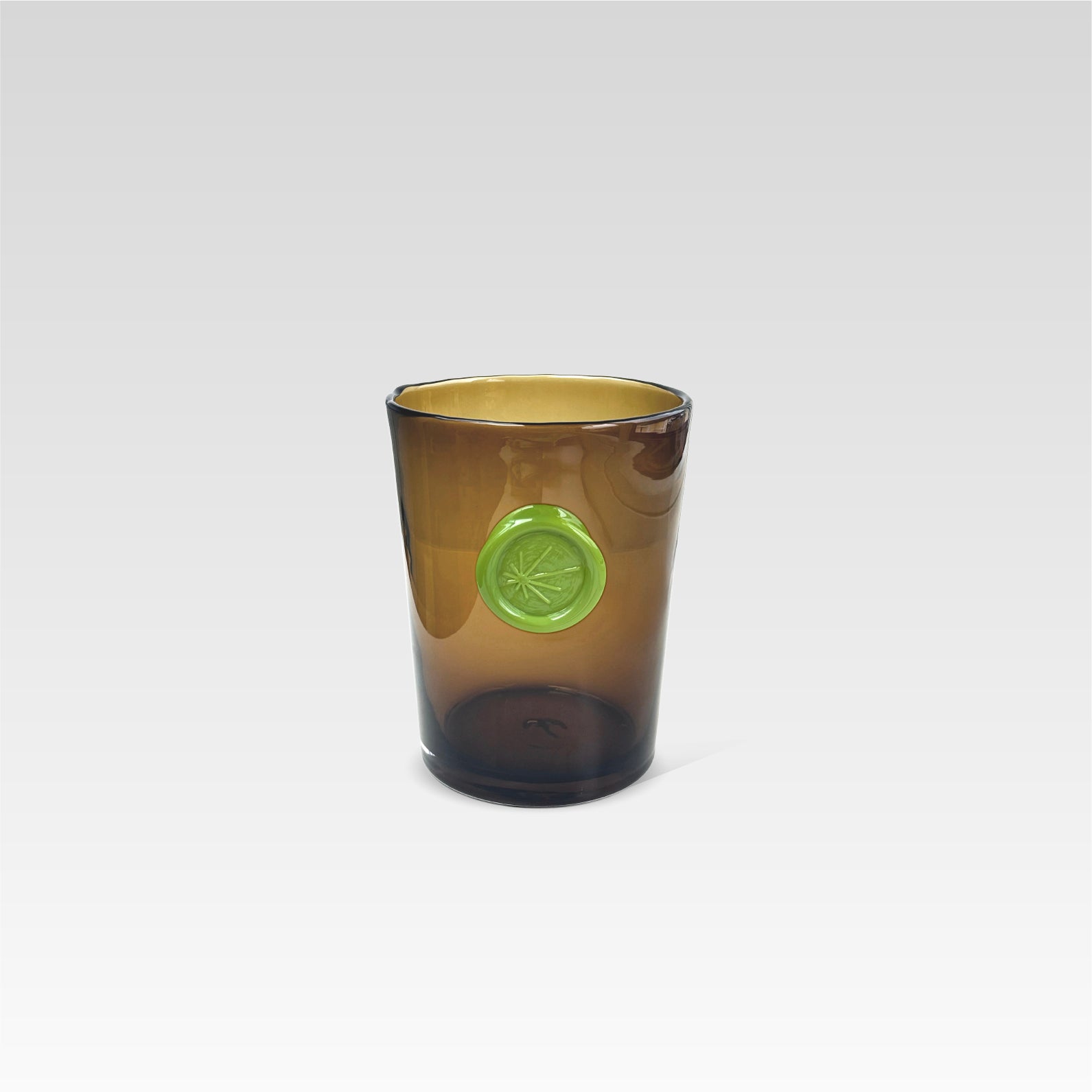 Brown glass tumbler with a green circular imprint design on the front, with a white background