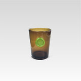 Brown glass tumbler with a green circular imprint design on the front, with a white background