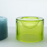 A translucent lime green wetbowl with a small recessed bowl inside, shown on a light gray surface with part of a blue wetbowl is visible on the left.