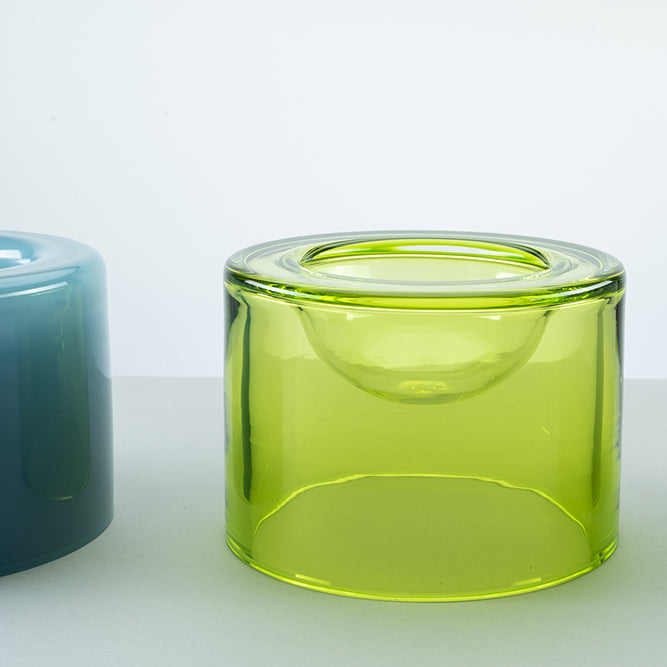 A translucent lime green wetbowl with a small recessed bowl inside, shown on a light gray surface with part of a blue wetbowl is visible on the left.