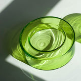 A translucent lime green wetbowl, photographed on a white surface with strong diagonal sunlight casting wonderful green shadows.