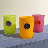 Three colorful glass vases with circular imprints in the middle of each of them, on a blue tinted wooden surface.