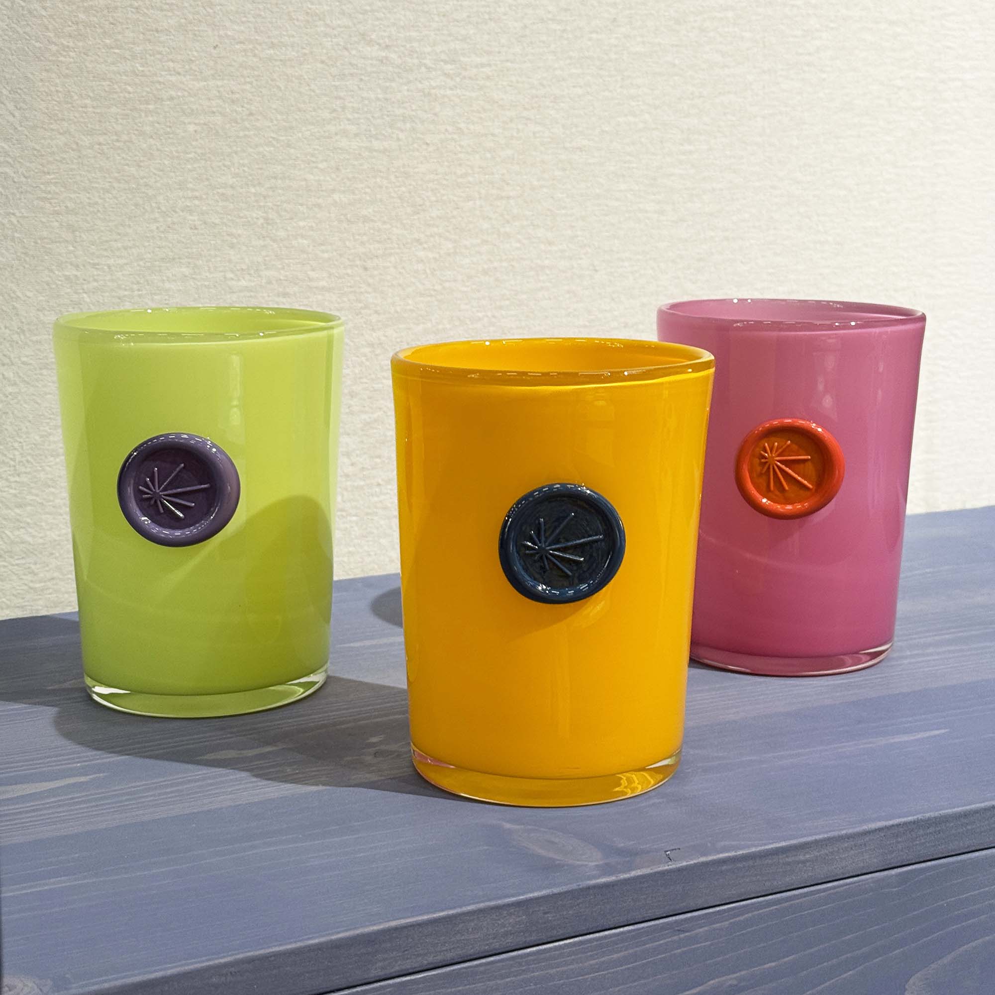 Three colorful glass vases with circular imprints in the middle of each of them, on a blue tinted wooden surface.