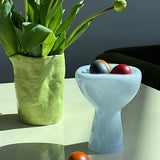 Green vase with tulips and colorful eggs inside a phantom dish on a reflective surface.