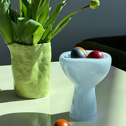 Green vase with tulips and colorful eggs inside a phantom dish on a reflective surface.