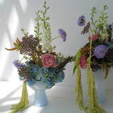 Two floral arrangements in light blue phantom dishes acting as vases on a white surface with a white background