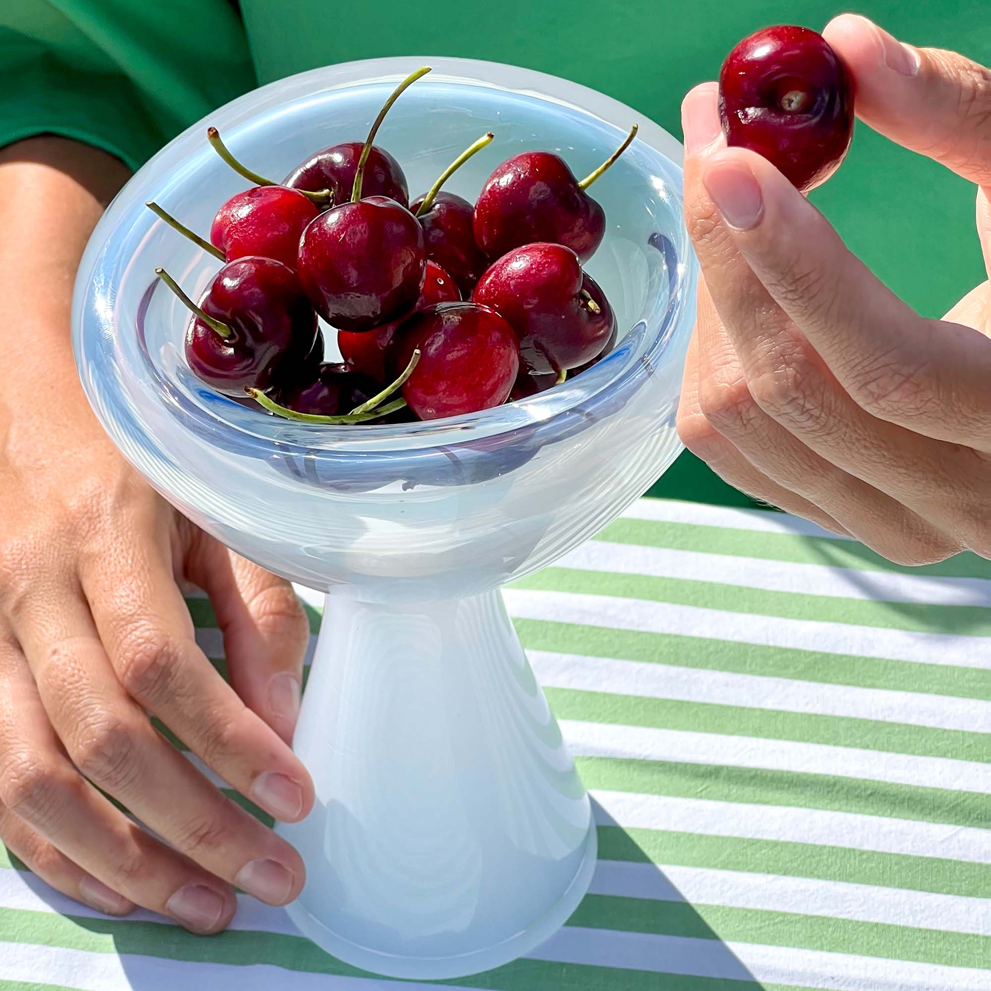 Person holding a bowl of cherries with a green background