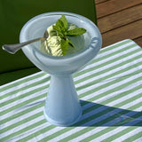 Green ice cream in a white bowl with a spoon on a striped tablecloth