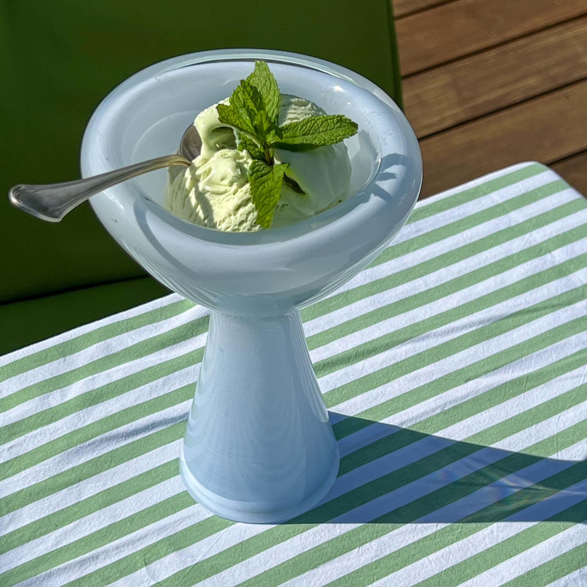 Green ice cream in a white bowl with a spoon on a striped tablecloth
