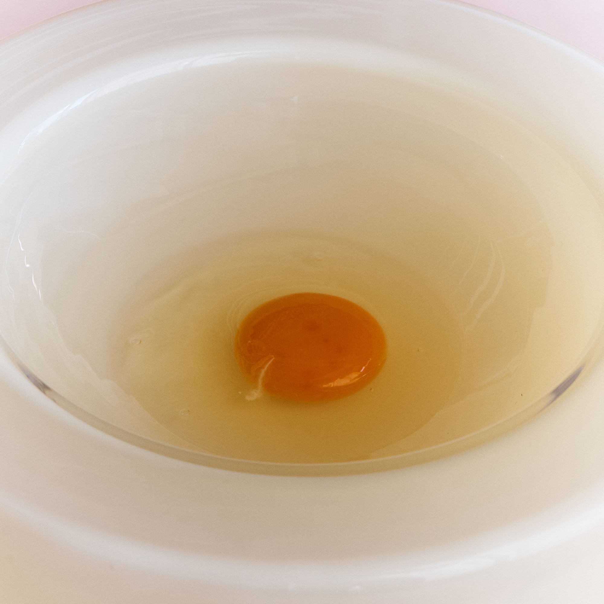 A cracked egg appears inside a white -vanilla bowl, closeup