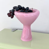 Pink glass bowl with grapes on a light green surface