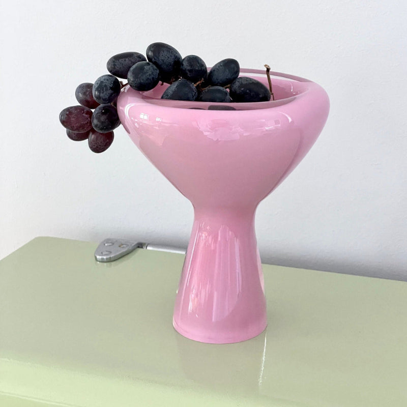 Pink glass bowl with grapes on a light green surface